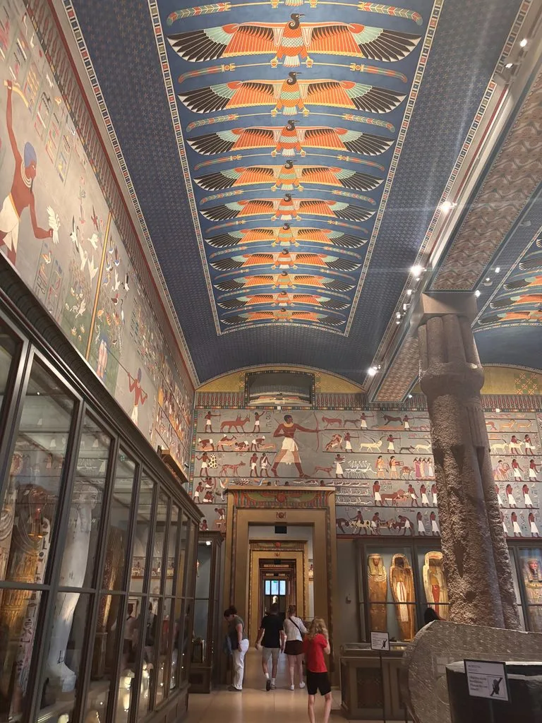 Interior of a grand museum gallery decorated with colorful ancient Egyptian-style murals, columns, and statues