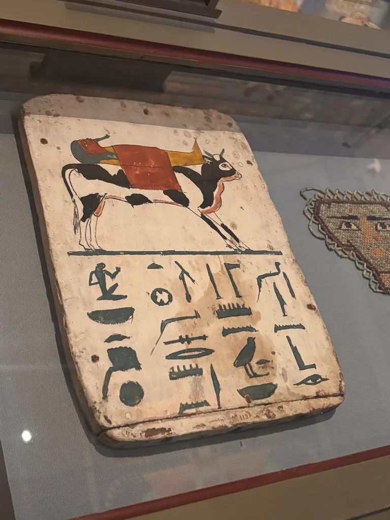 Egyptian artifact: Close-up of an ancient Egyptian tablet covered with black hieroglyphic symbols, displayed behind glass in a museum.
