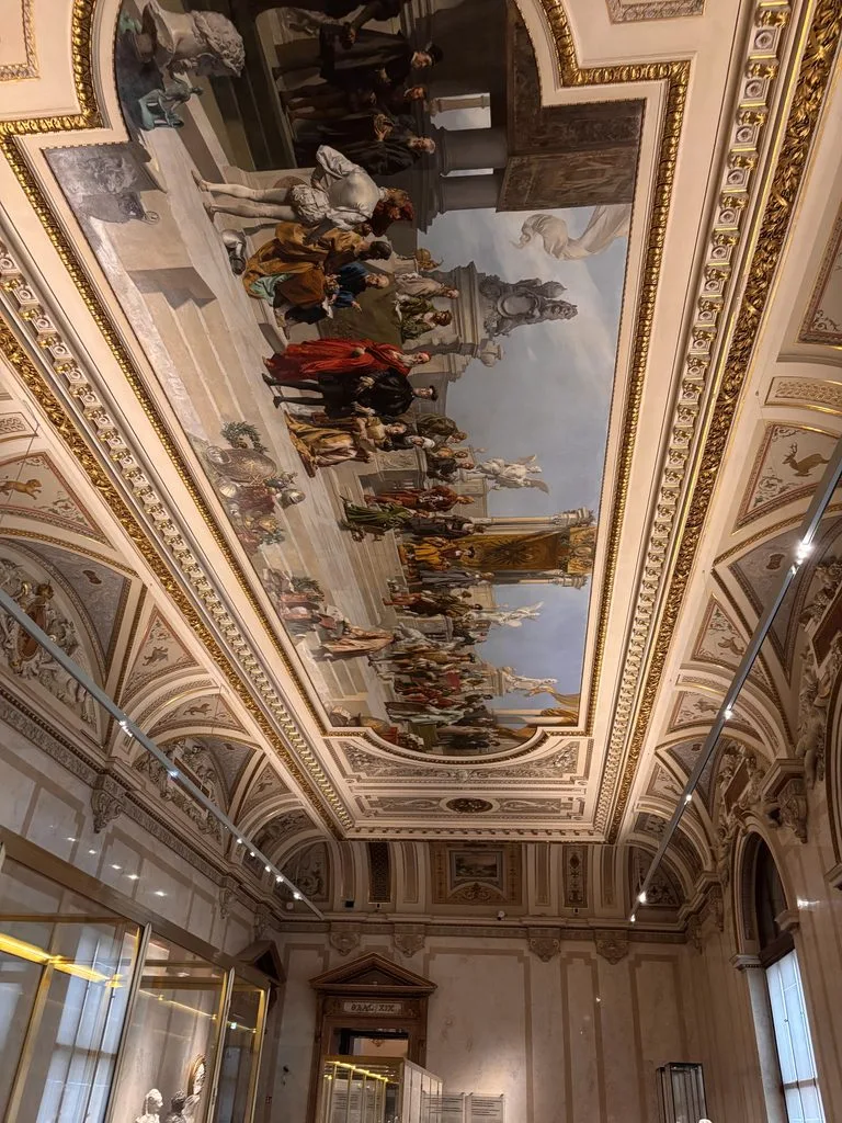 ecorated museum ceiling: Detailed view of an elaborate painted ceiling featuring historical and mythological scenes, surrounded by ornate gold and architectural decoration.