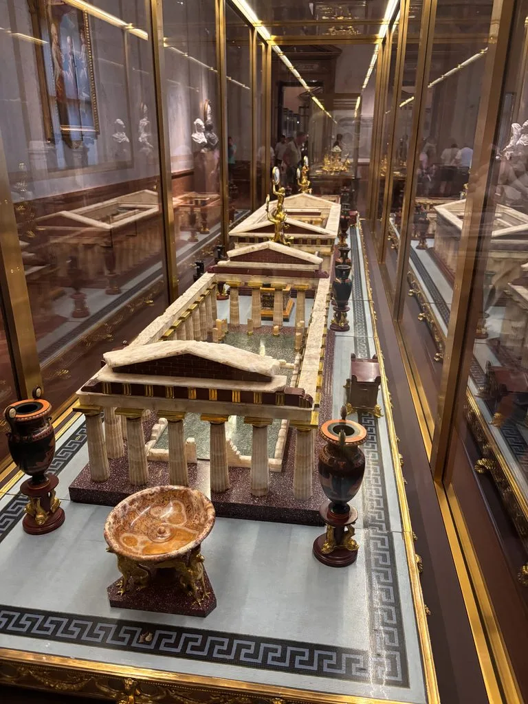 Ancient Roman model: Detailed miniature model of an ancient Roman-style temple or architectural structure displayed in a glass museum case, surrounded by decorative objects